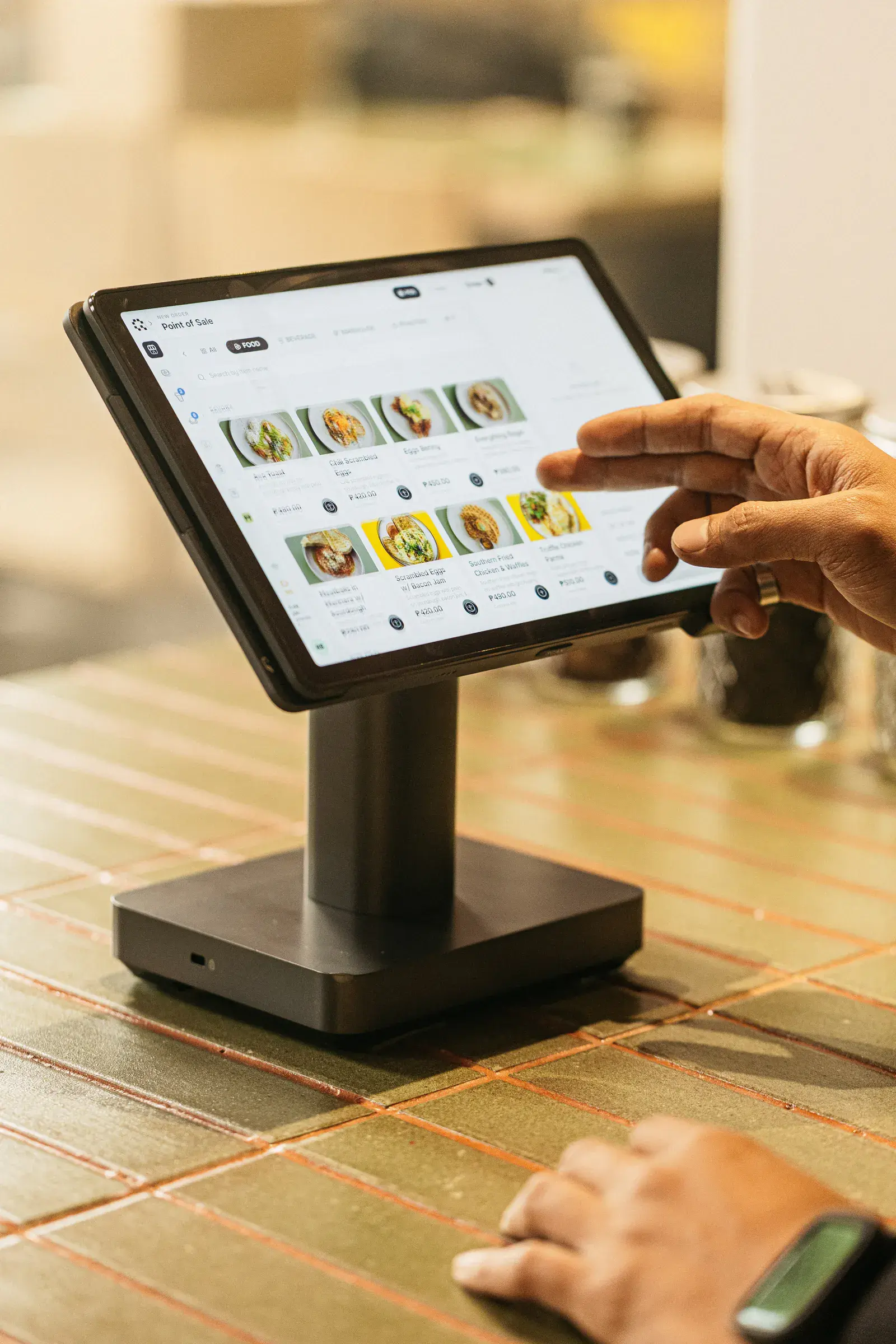 A hand tapping the menu on a counter terminal