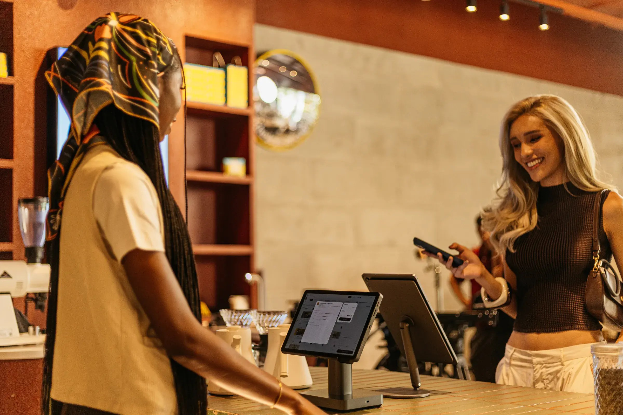 A barista and a customer with a phone at a café counter, two counter terminals between them