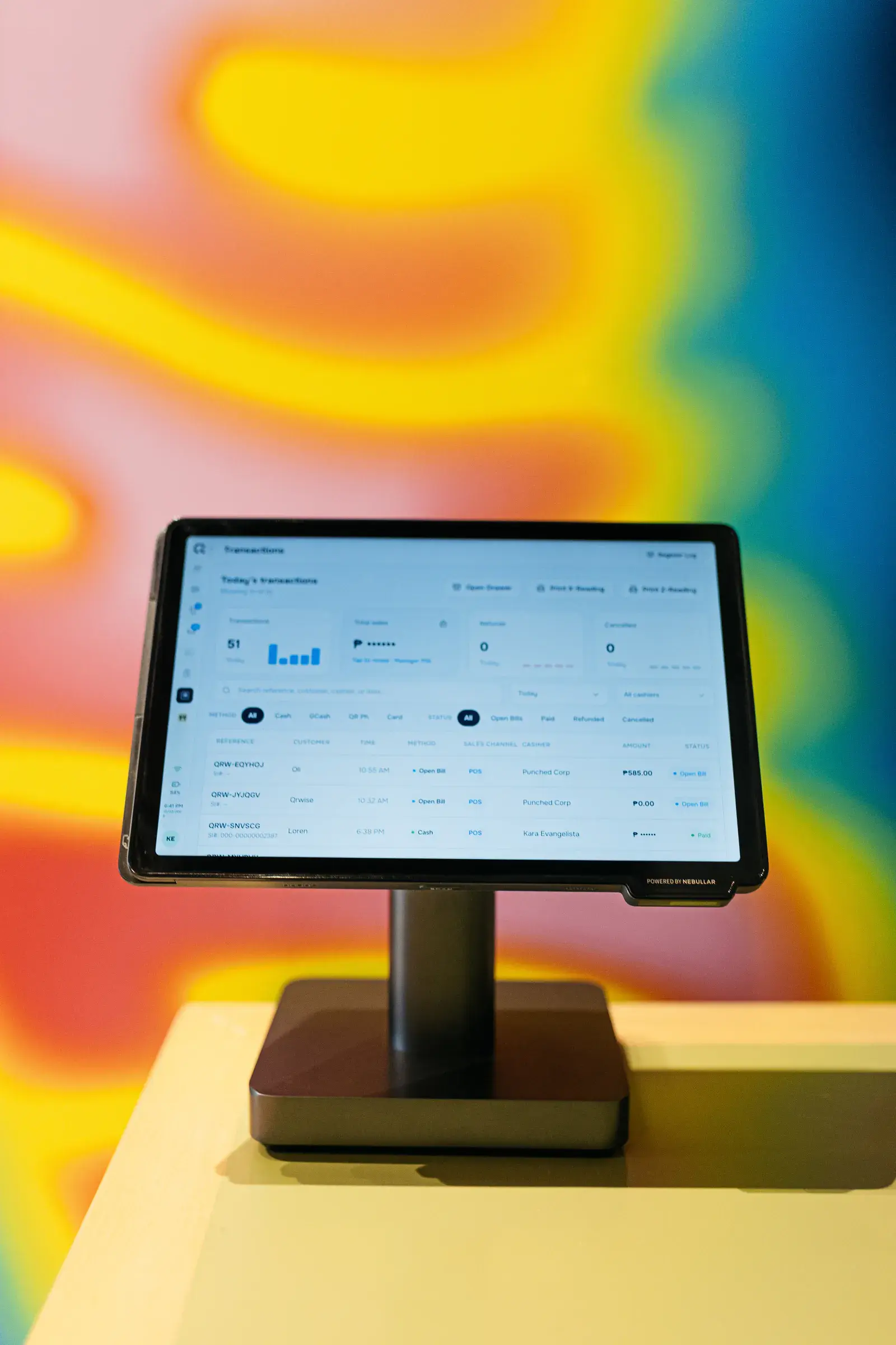 A counter terminal showing a transactions dashboard against a colourful backdrop