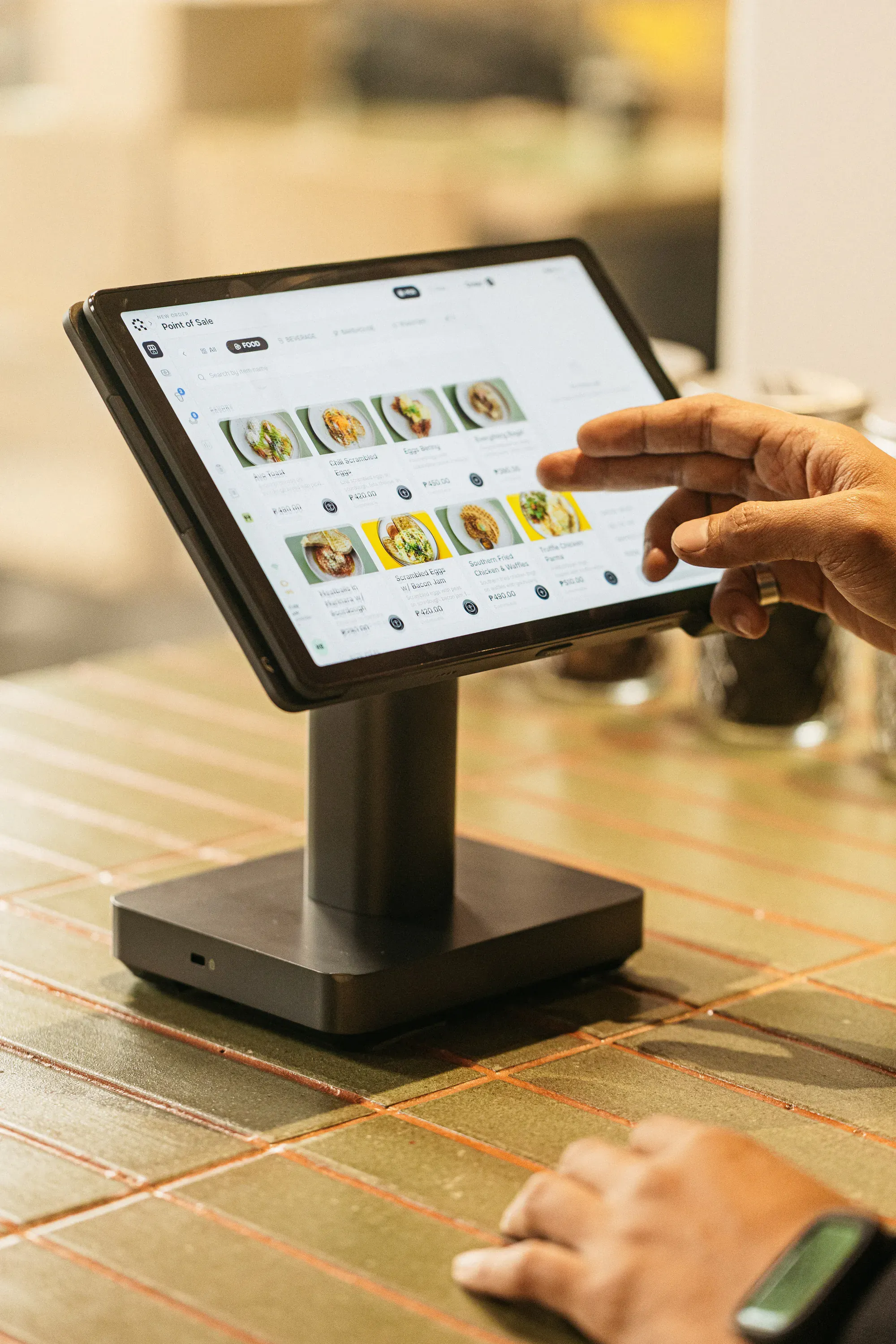 A hand tapping the menu on a counter terminal